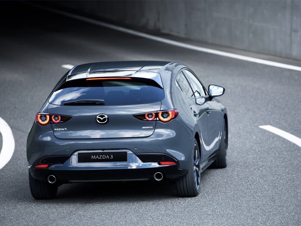 Deep Crystal Blue Mica Mazda3 Sport seen from behind and above, drives into a tunnel.