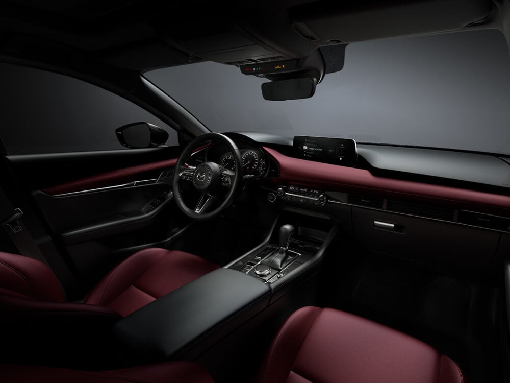 Plan studio du garnissage en cuir rouge grenat montrant le siège conducteur, le tableau de bord, la console et une partie du siège passager avant d’une Mazda3 Sport.