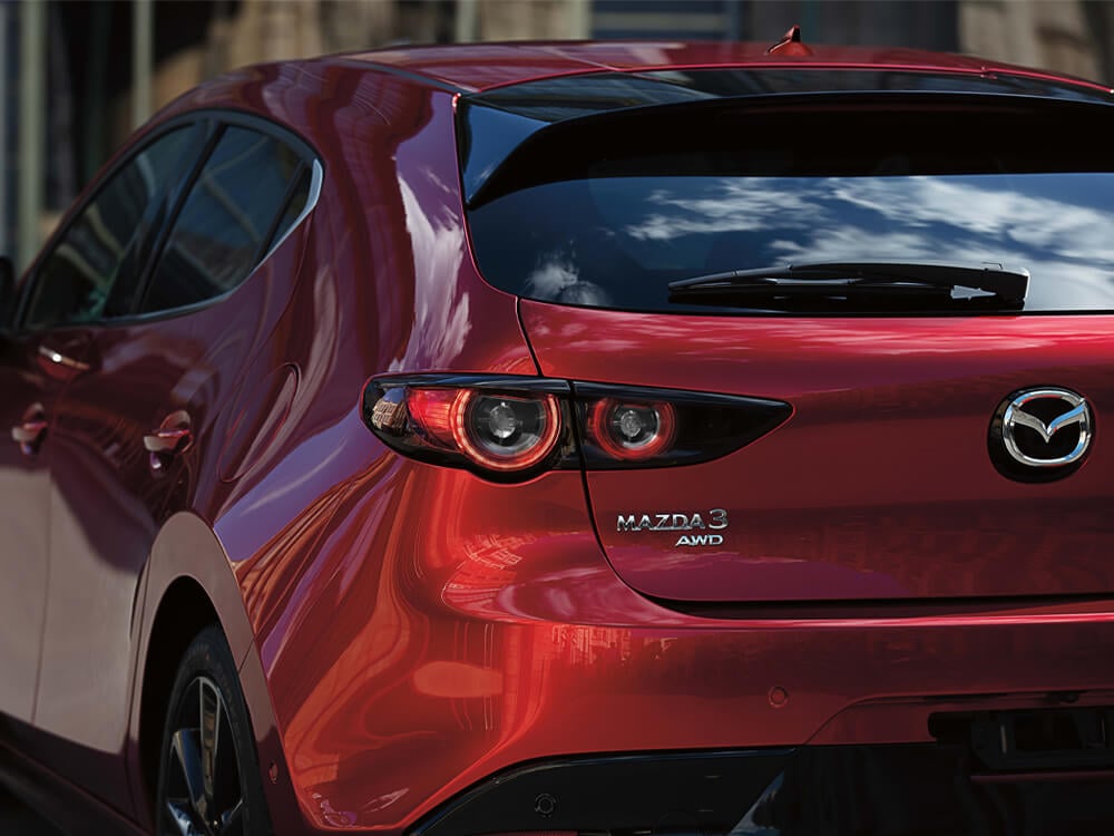 Gros plan des emblèmes Mazda3 et AWD et du logo Mazda sur le hayon d’une Mazda3 Sport rouge vibrant cristal métallisé.