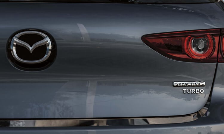 Gros plan de l’emblème Skyactiv-G TURBO et du logo Mazda sur le hayon. 