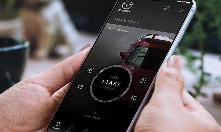 Hands holding smartphone with MyMazda app. 
