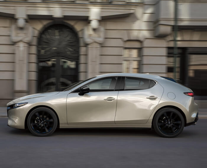Mazda3 Sport drives down city street, passing a hotel’s large arched entryway.