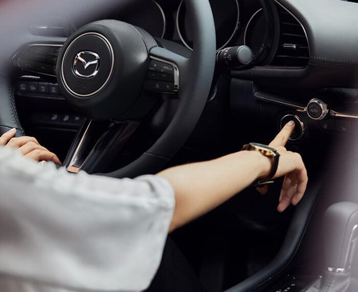 Gros plan du volant et de l’intérieur d’une Mazda3 Sport; la main du conducteur appuie sur le bouton de démarrage du moteur.  