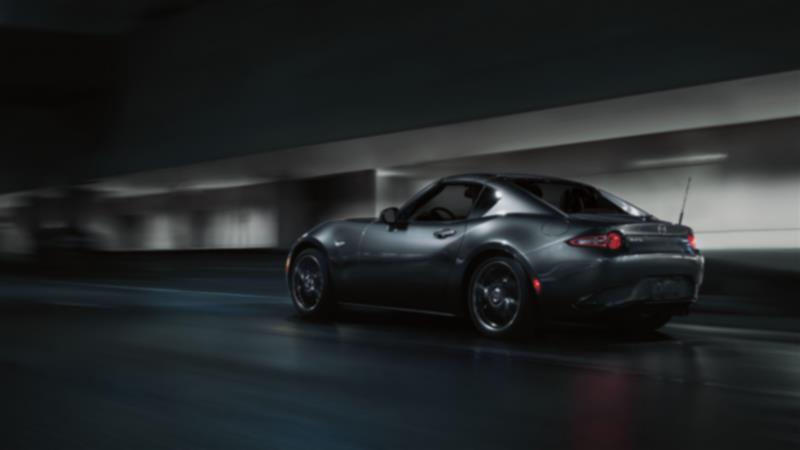 A dark MX-5 RF drives down a city road at night. 