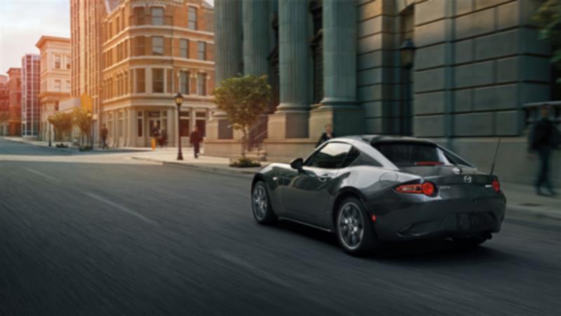 A silver MX-5 RF drives down a city street. 