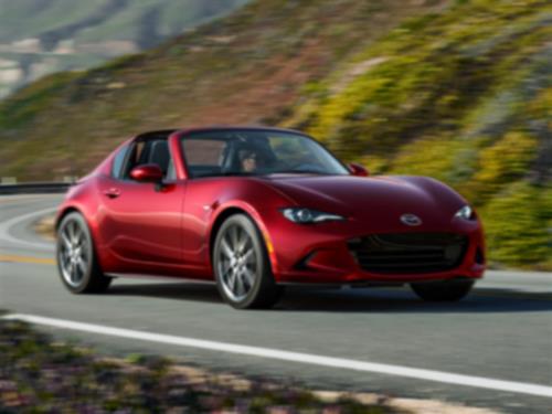 A red MX-5 RF drives down a winding road with scenery blurred in the background. 