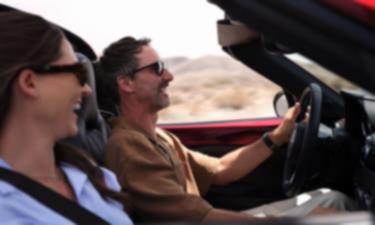 Deux personnes souriantes portant des lunettes de soleil roulent sur une route dans une MX-5 RF rouge.