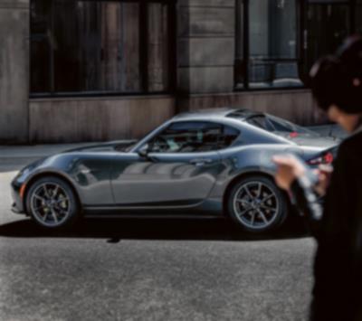 A metallic, reflective MX-5 RF sits parked on a city street.