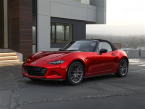 Vue de 3/4 d’une MX-5 ST rouge avec le toit fermé garée devant une maison moderne.