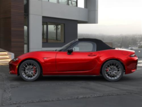 Vue latérale d’une MX-5 ST rouge avec le toit fermé garée devant une maison moderne.