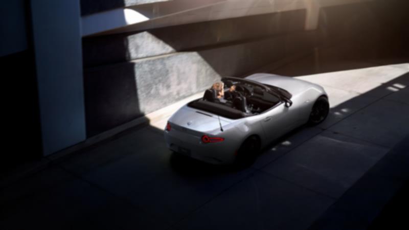 A person drives an MX-5 ST with the top down in the city.