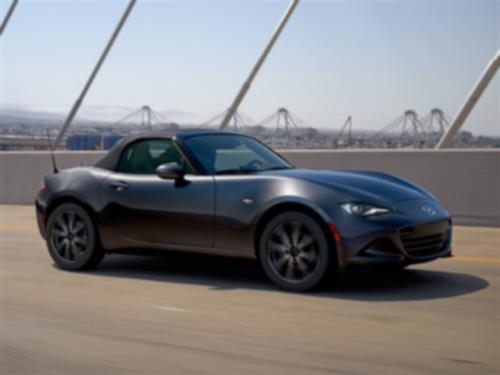 Dark MX-5 ST with the top up drives across a bridge.