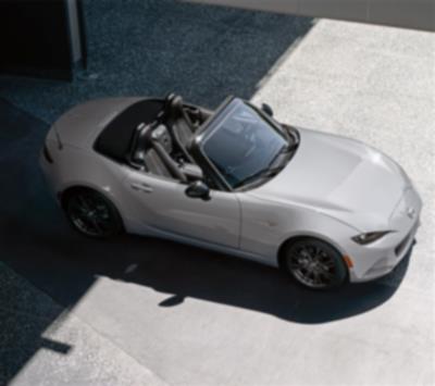 A sliver MX-5 ST parked half in the shade and half in sunlight.