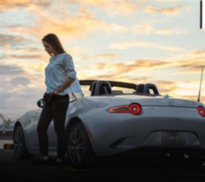 Un conducteur, la main dans la poche, se tient à côté d’une MX-5 ST argent.