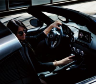 A driver in sunglasses uses their right hand to adjust settings on the dashboard controls.