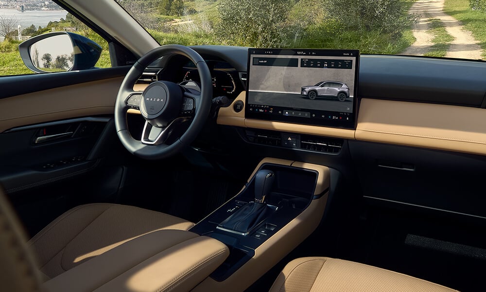 View from the front passenger seat of a Mazda CX-5, showing the steering wheel and centre touchscreen display.
