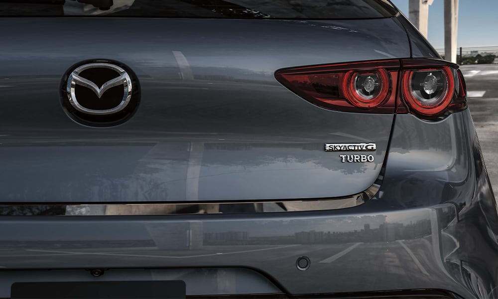 View through the panoramic moonroof of a Mazda3 Sport, looking down at a hand resting on the centre control knob.